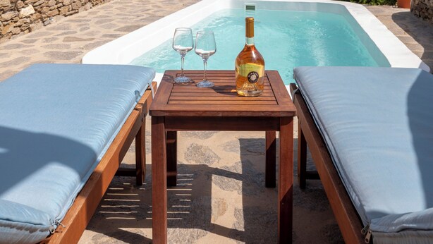 A poolside area with a table, two lounge chairs, and a bottle of wine. - Πολυτελής σουιτα με ιδιωτικη πισινα και υπέροχη θέα στο Αιγαίο! (Paros)