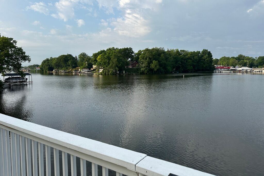 A calm lake with a dock and a white railing in the foreground.