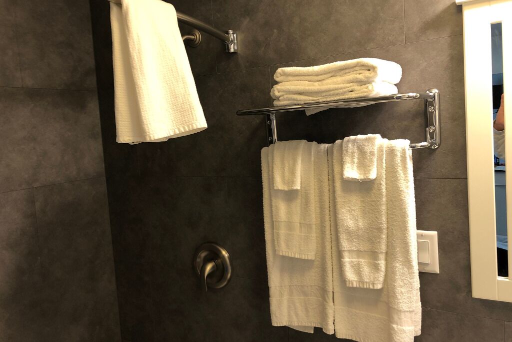 Une salle de bain aux murs sombres, avec une porte de douche et un porte-serviettes sur lequel sont pliées plusieurs serviettes.