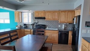 A modern kitchen with wooden cabinets, a black refrigerator, and a dining area with a wooden table and chairs. - 3 Bedroom Suite, just steps from Indiana Beach with lake access and more! (Monticello)