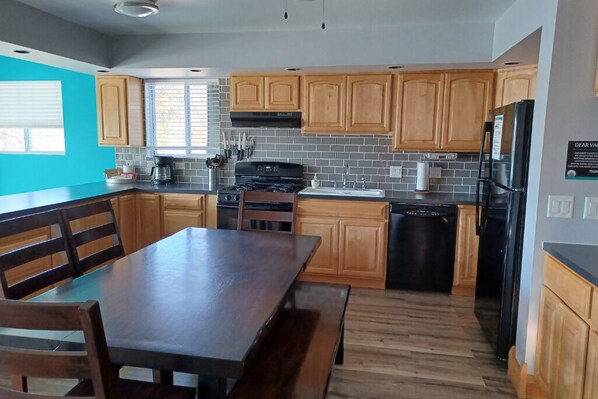 Una cocina moderna con armarios de madera, un refrigerador negro y una zona de comedor con mesa y sillas de madera.
