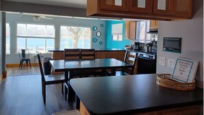 A modern kitchen with wooden cabinets, a dining area with a black table and chairs, and a view of the outside through large windows. - 3 Bedroom Suite, just steps from Indiana Beach with lake access and more! (Monticello)