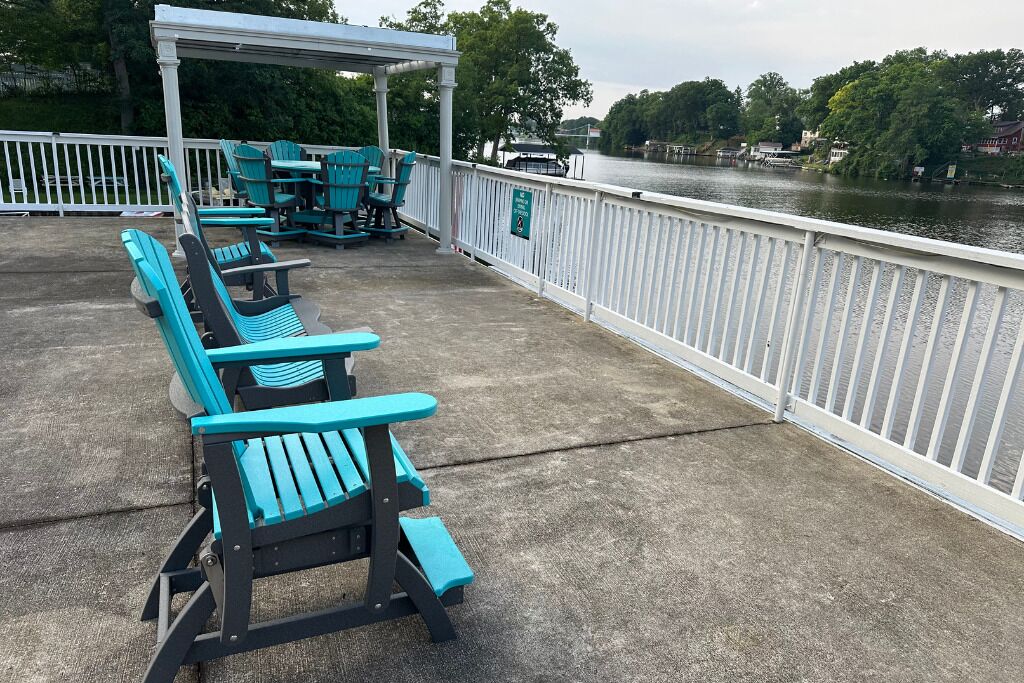 Un espace extérieur aménagé, abrité et doté de chaises Adirondack turquoise et d’une table de pique-nique, offrant une vue sur une rivière.