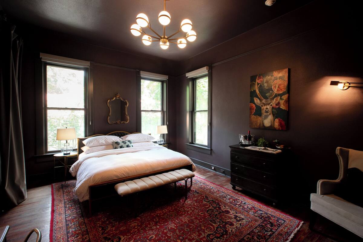 Una camera da letto con un letto grande, un tappeto rosso decorato, un lampadario e un quadro raffigurante un cervo.
