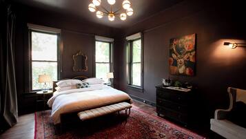 Un dormitorio con una cama grande, un tapete rojo estampado, una araña y una pintura de un ciervo en la pared.