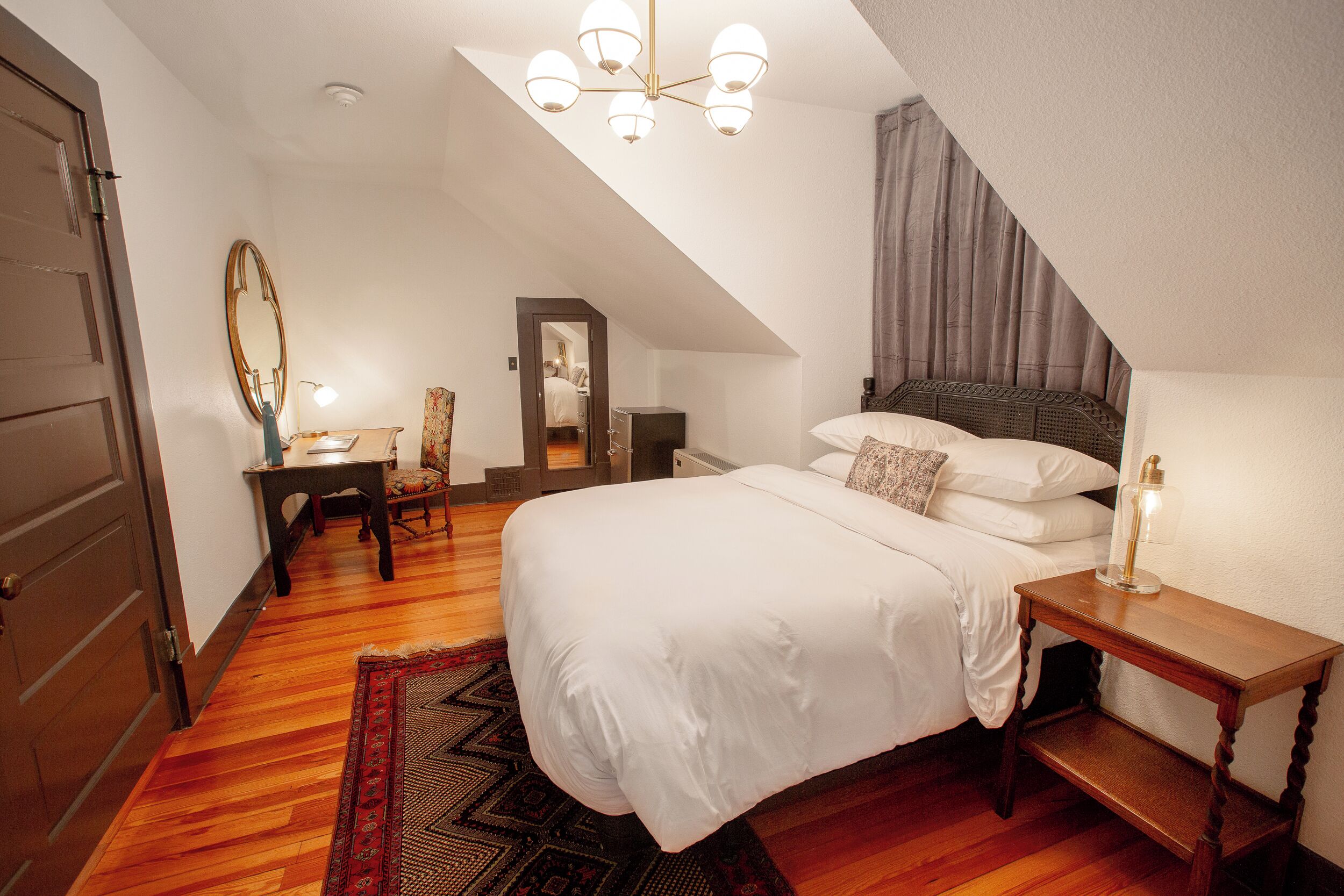 Une chambre à coucher avec un grand lit, une table de chevet en bois, une chaise, un bureau et un miroir.