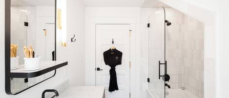 A modern bathroom with a white sink, black faucet, and a glass shower enclosure.