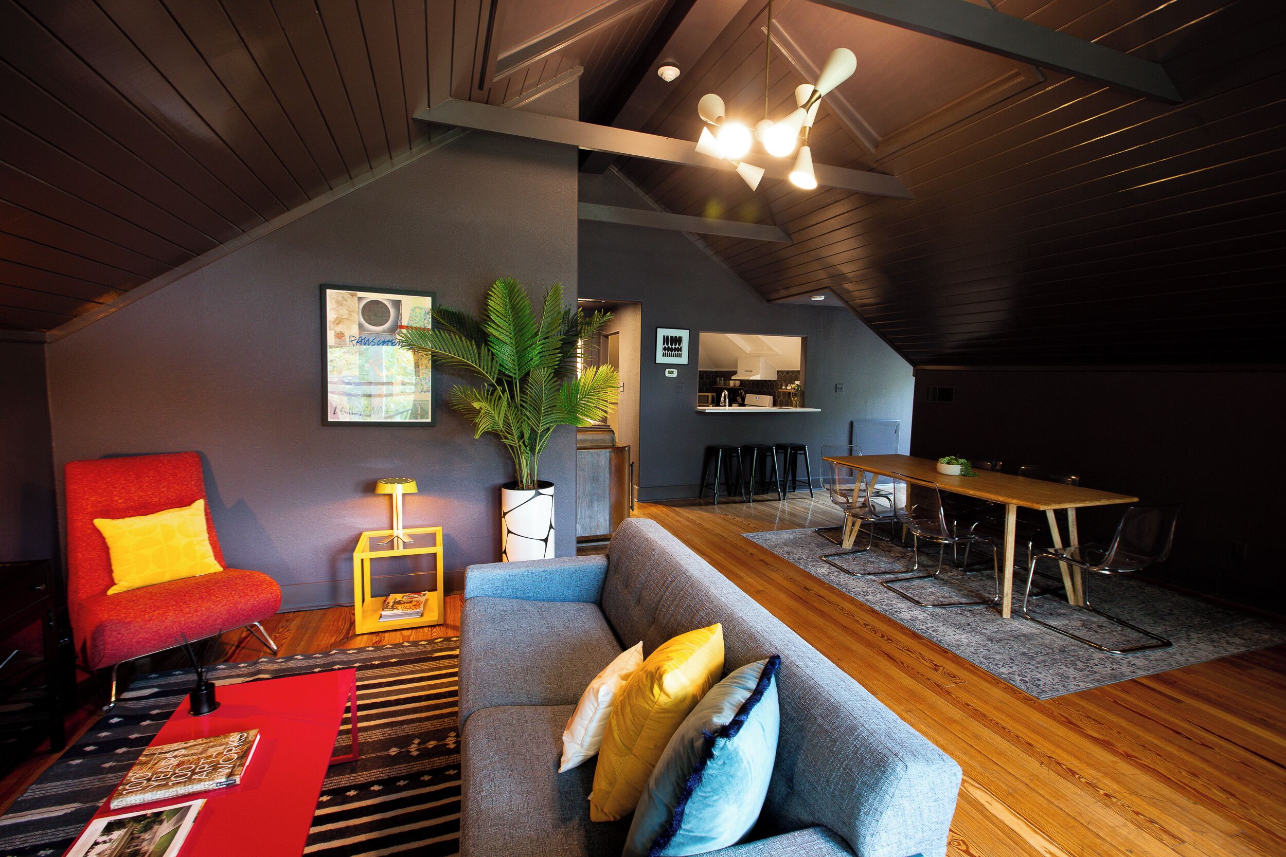 A modern living room with a grey sofa, red armchair, and a wooden dining table.