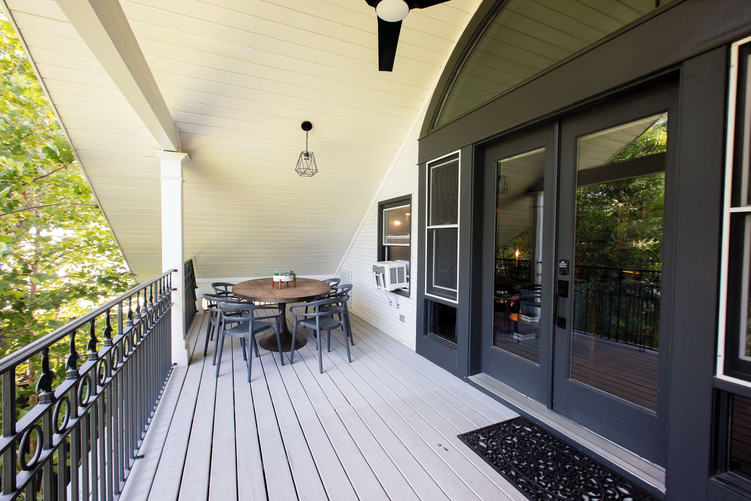 A covered porch with a table and chairs, large windows, and a black metal railing.