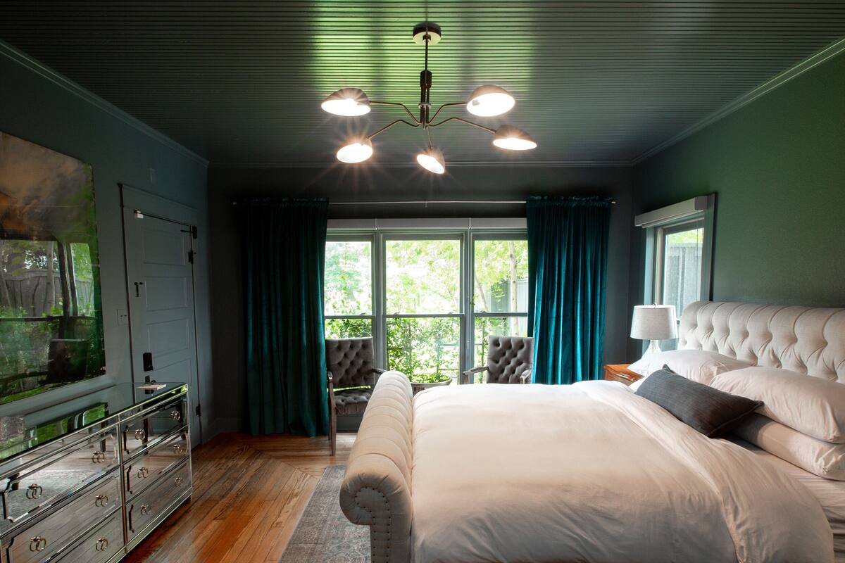 Una camera da letto con un letto grande, una cassettiera, un lampadario e vista sull'esterno attraverso la finestra.