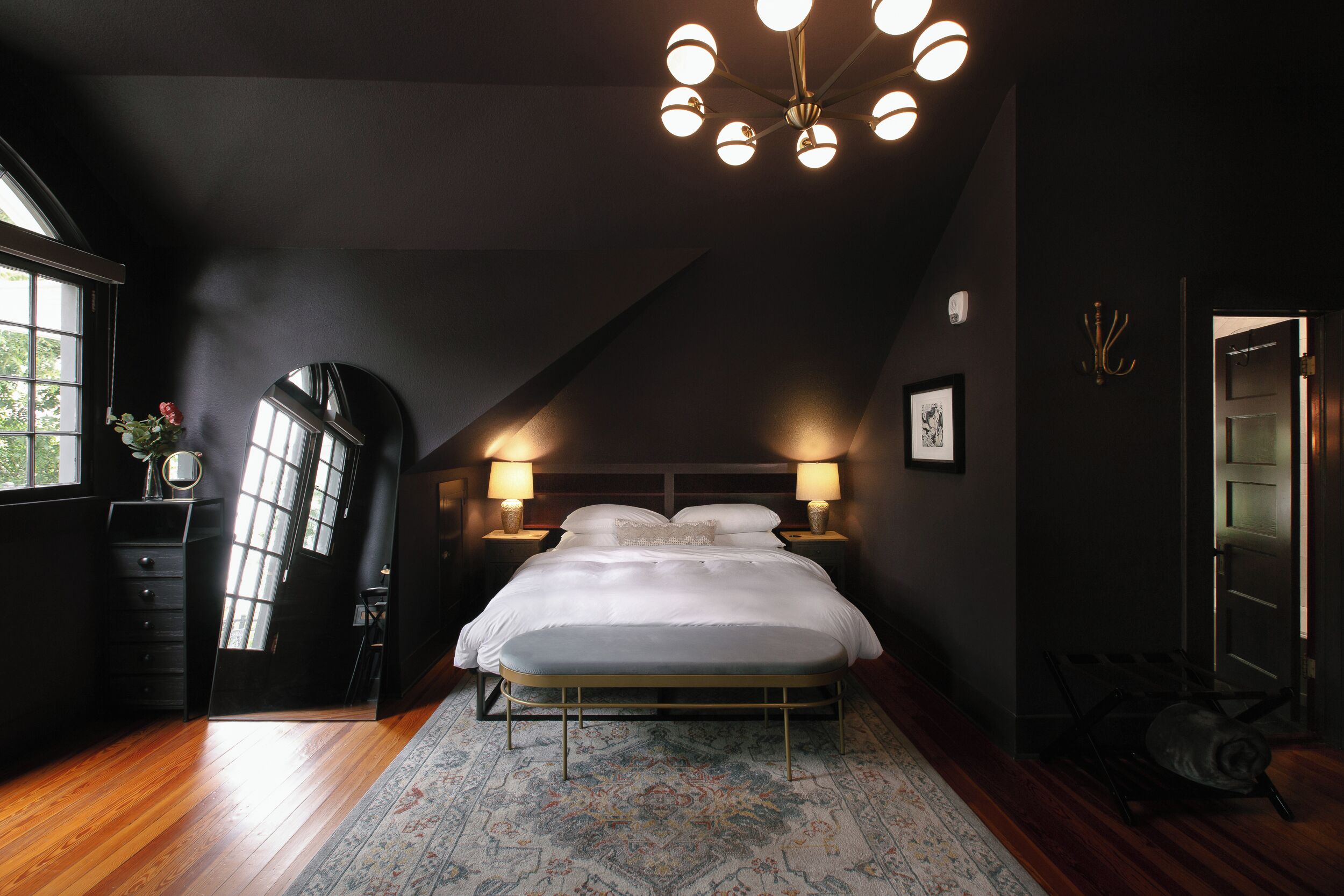 Ein Schlafzimmer mit einem großen Bett, zwei Nachttischlampen, einem Spiegel und einem Fenster.