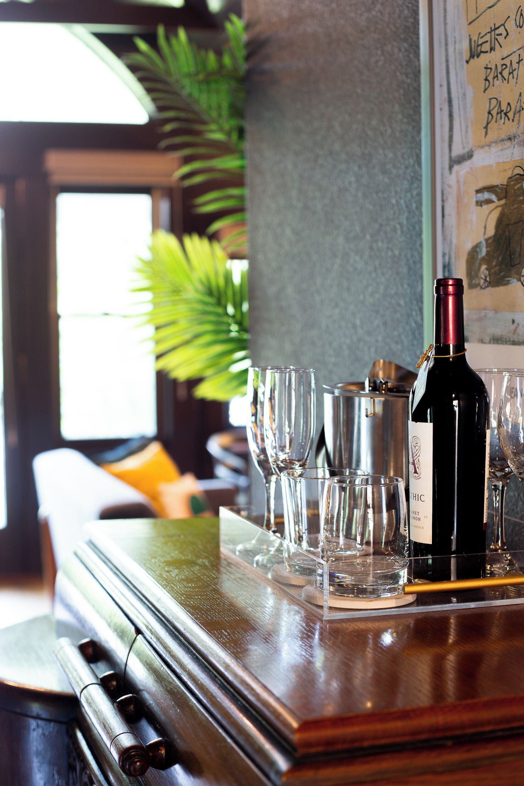 Un coin bar avec une bouteille de vin, des verres et un récipient en métal posés sur un comptoir en bois.