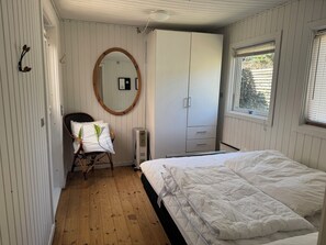 A bedroom with a bed, a chair, a wardrobe, a mirror, and a window. - Cottage at Nordstrand (Nykøbing Sj)