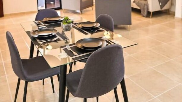A dining area with a glass table, black chairs, and a modern sofa in the background. - Rango #3 – Your Perfect Space in Cabrera (Cabrera)