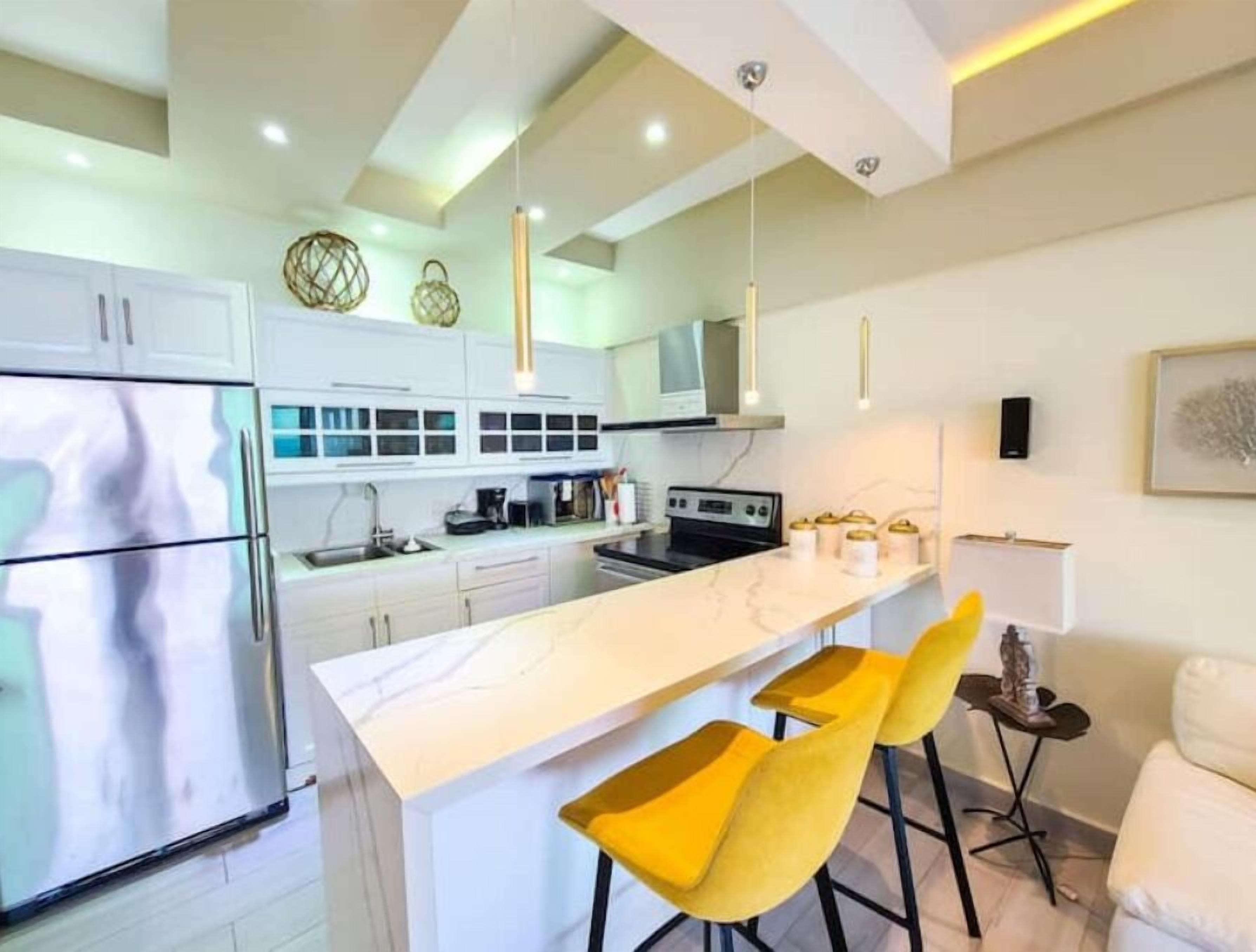 A modern kitchen with white cabinets, a marble countertop, and yellow bar stools.