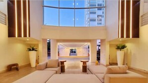 A spacious lobby with a large sectional sofa, two side tables, and a central coffee table. There are tall, narrow windows on the sides and a large skylight above.