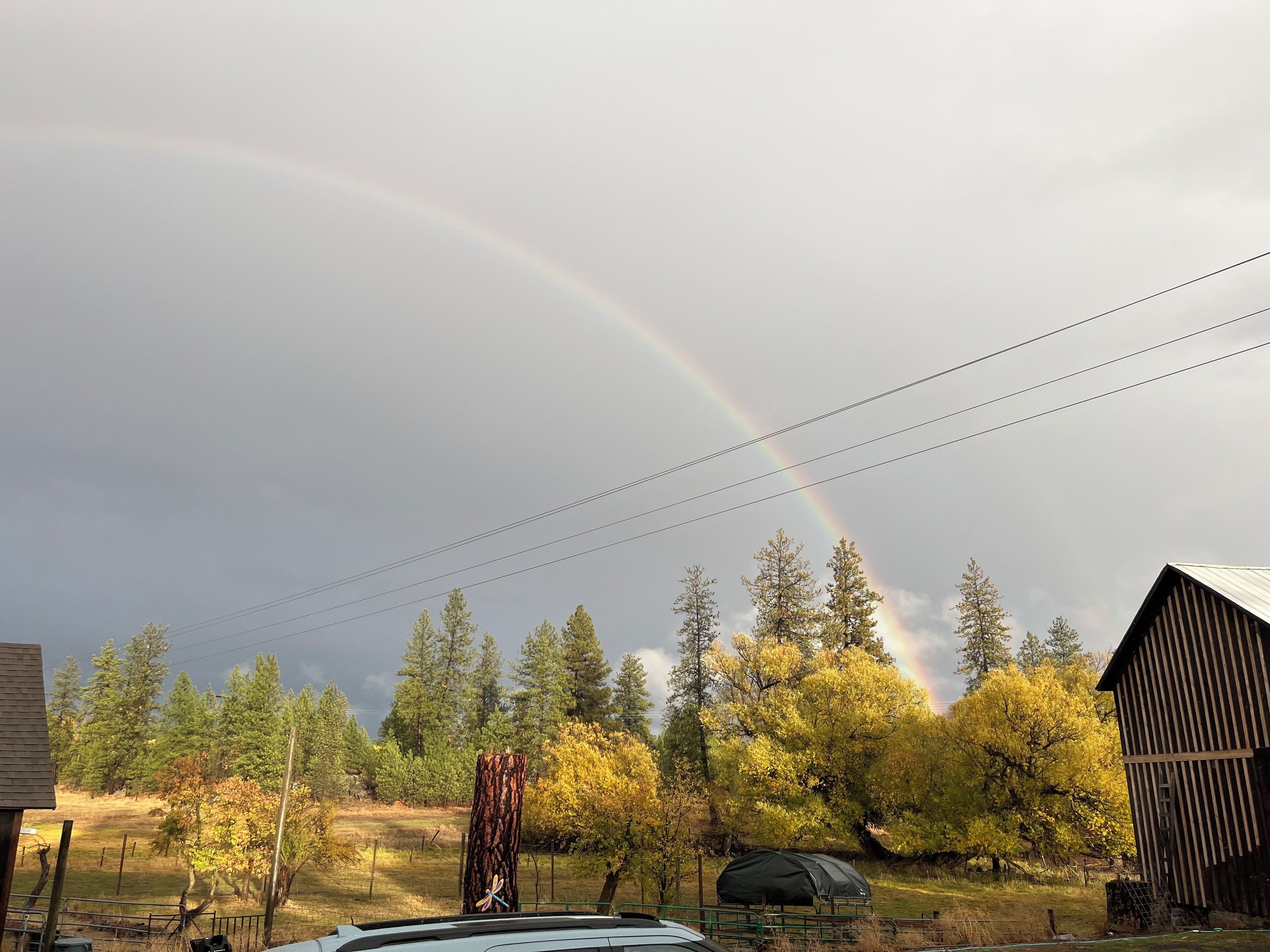 A rural landscape with a rainbow, a barn, and a tent.
