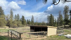 A small, single-story building with a sloped roof, surrounded by a fenced area with a gate. - The Cottage at Dragonfly Meadows Farm with AC and wifi (Cheney)