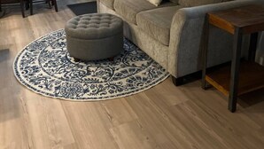 A living room with a grey sofa, a round ottoman, a patterned rug, a wooden coffee table, and an air conditioning unit on the wall. - The Cottage at Dragonfly Meadows Farm with AC and wifi (Cheney)