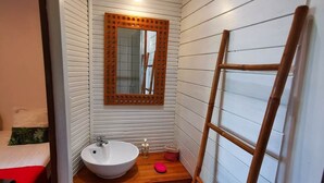 Een kleine badkamer met een witte wastafel, houten wastafelmeubel en een spiegel met houten lijst.