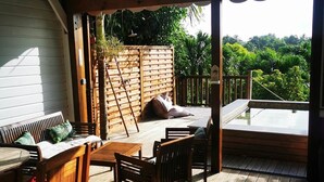 Een houten terras met een tafel en stoelen, een plafondventilator en uitzicht op weelderige begroeiing.