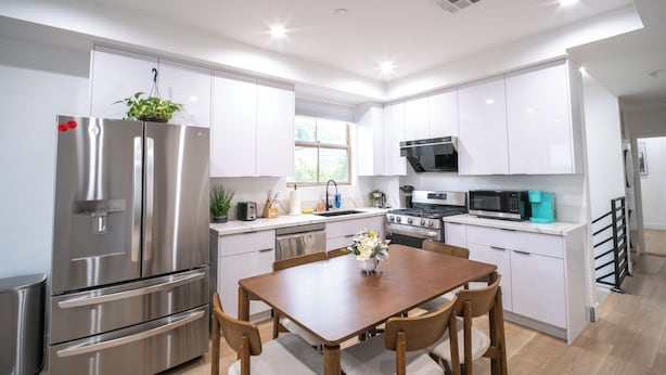 Una cocina moderna con armarios blancos, electrodomésticos de acero inoxidable y una mesa de comedor de madera.