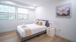 Un dormitorio moderno con una cama grande, mesitas de noche y una ventana con persianas.