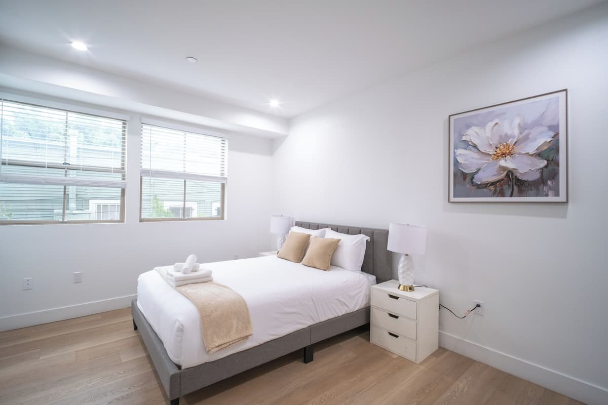Une chambre moderne avec un grand lit, des tables de chevet et une fenêtre équipée de stores.