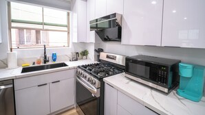 Una cocina moderna con armarios blancos, una estufa de acero inoxidable, un microondas y una cafetera.