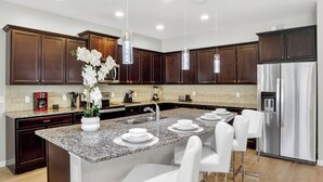 A modern kitchen with dark wooden cabinets, a granite countertop, stainless steel appliances, and white bar stools.