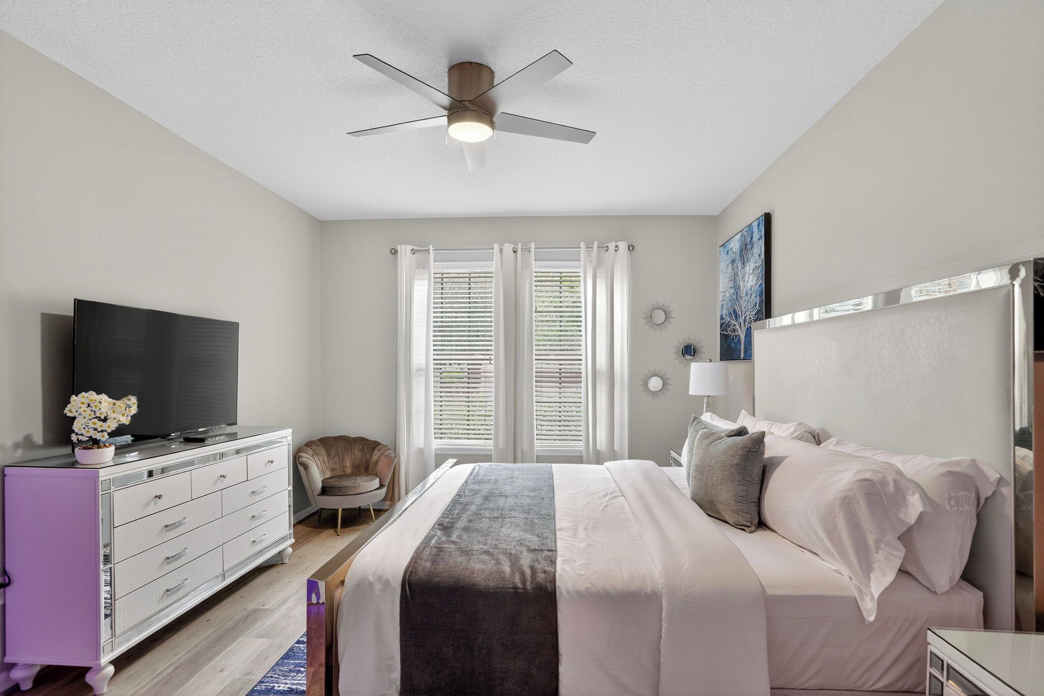 A bedroom with a bed, a dresser, a television, a ceiling fan, and a window with blinds.