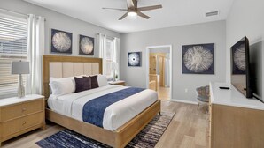 A modern bedroom with a large bed, a ceiling fan, and artwork on the walls.