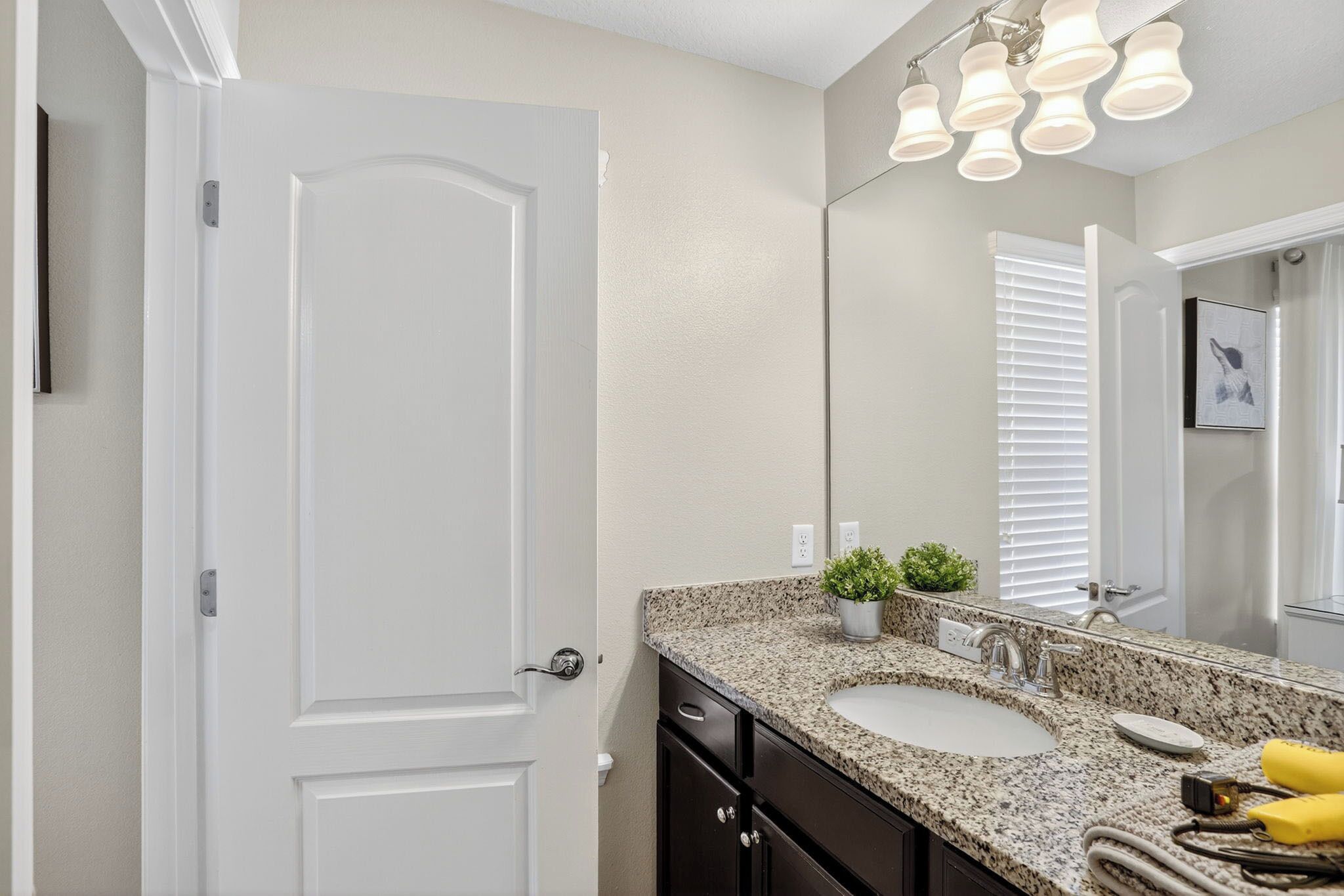 A bathroom with a white door, a granite countertop sink, a mirror, and a ceiling light fixture.