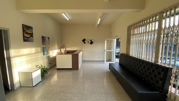 A spacious lobby with a reception desk, a black sofa, and artwork on the walls. - Pousada Central Campo Largo (Campo Largo)