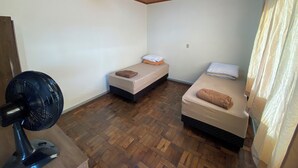 A small, compact room with two single beds, a standing fan, and a wooden ceiling. - Pousada Central Campo Largo (Campo Largo)