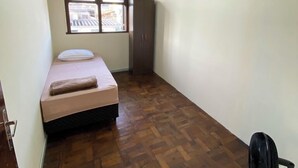 A small, sparsely furnished room with a wooden floor, a single bed, a window, and a fan. - Pousada Central Campo Largo (Campo Largo)