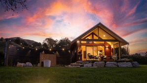 Une cabane moderne dotée d’une grande porte vitrée, d’un coin repas avec des sièges extérieurs et d’un chemin en pierre menant à l’entrée.