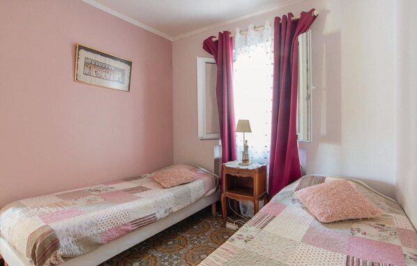A bedroom with two single beds, a small wooden nightstand, a lamp, and a framed picture on the wall.