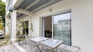 An outdoor patio with a table and chairs, a sliding glass door, and a view of the street. - Appartement Proche Plage (La Rochelle)