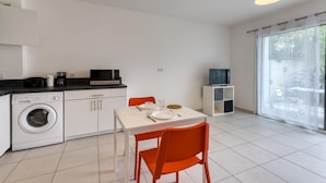 A compact kitchen with a washing machine, microwave, and coffee maker, a dining table with chairs, and a TV on a stand. - Appartement Proche Plage (La Rochelle)