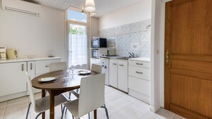 A kitchen with a dining table, chairs, a wooden door, and a window with a view. - 1 bedroom cozy home in La Rochelle (La Rochelle)