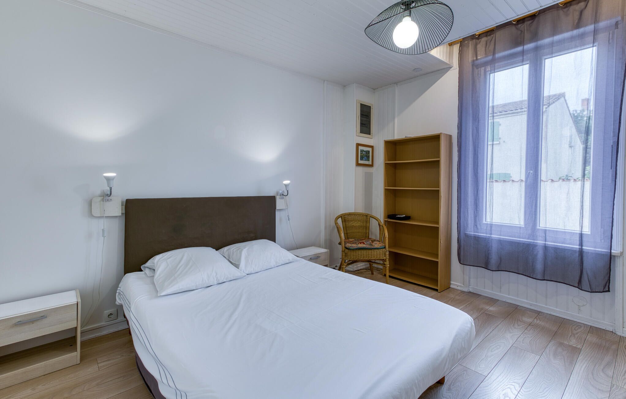 Un dormitorio con cama, una silla, un armario y una ventana con cortinas.