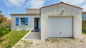 Una pequeña casa con garaje, una puerta y una ventana con contraventanas azules.