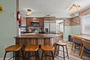 A kitchen with a central island, bar stools, wooden cabinets, stainless steel appliances, and a brick accent wall. - 6BR Waterfront • Direct Gulf • Fire Pit • Biliards (Hernando Beach)