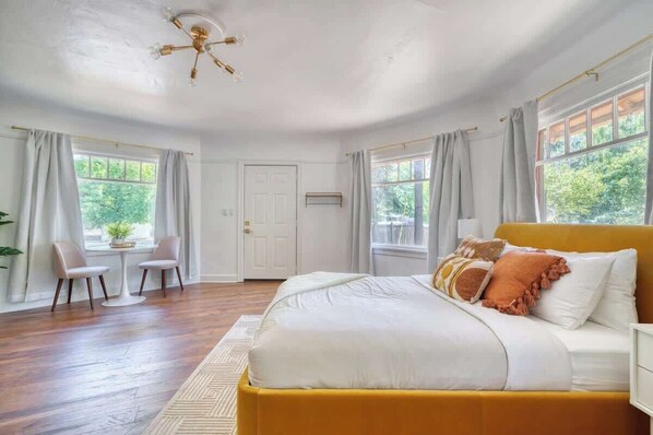 A bedroom with a large bed, a yellow headboard, and a view of greenery outside.