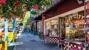 A street view with outdoor seating, a cafe, and a storefront with a neon sign. - Forest Studio Oasis - Mile from Multnomah Village (Portland)