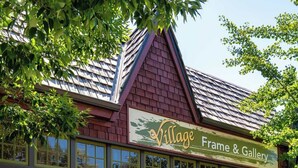 Fachada de loja com o nome 'Village Frame & Gallery', possui toldo verde e frontão de tijolos.