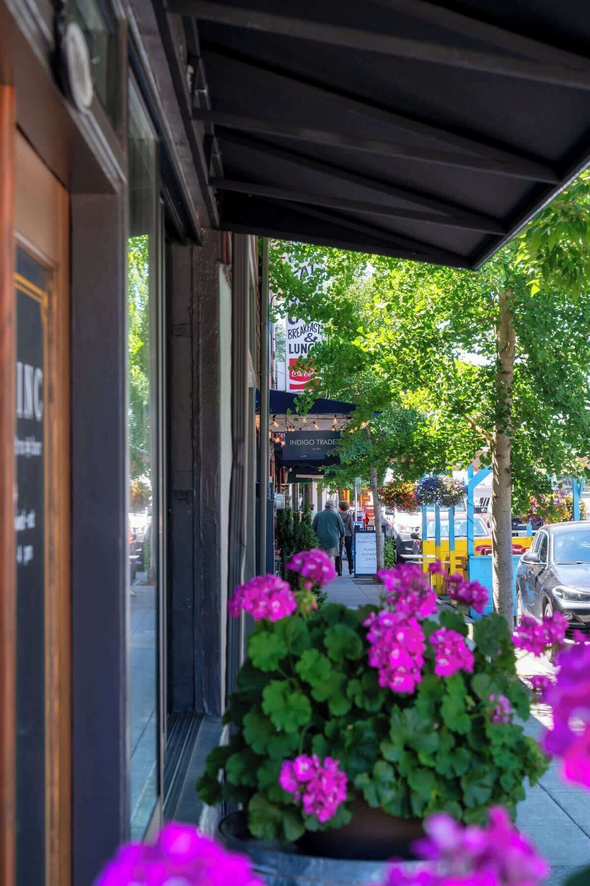 A storefront with a sign for breakfast and lunch, a planter with pink flowers, and a tree in the foreground.