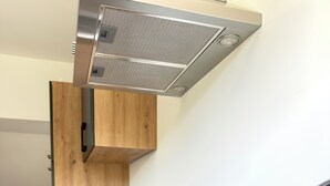 Une cuisine moderne dotée d’une cuisinière intégrée, de meubles en bois, d’une hotte en acier inoxydable, d’un petit évier et d’une plante en pot.