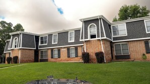 A two-story residential building with a brick facade, multiple windows, and a well-maintained lawn. - Cozy 1BR Condo - Pool & Wi-Fi (Osage Beach)